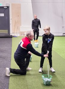 Ebi Kettunen opastaa Aaronia hyvään alkuasentoon Ollin harjoitellessa avauslyöntiä taaempana.