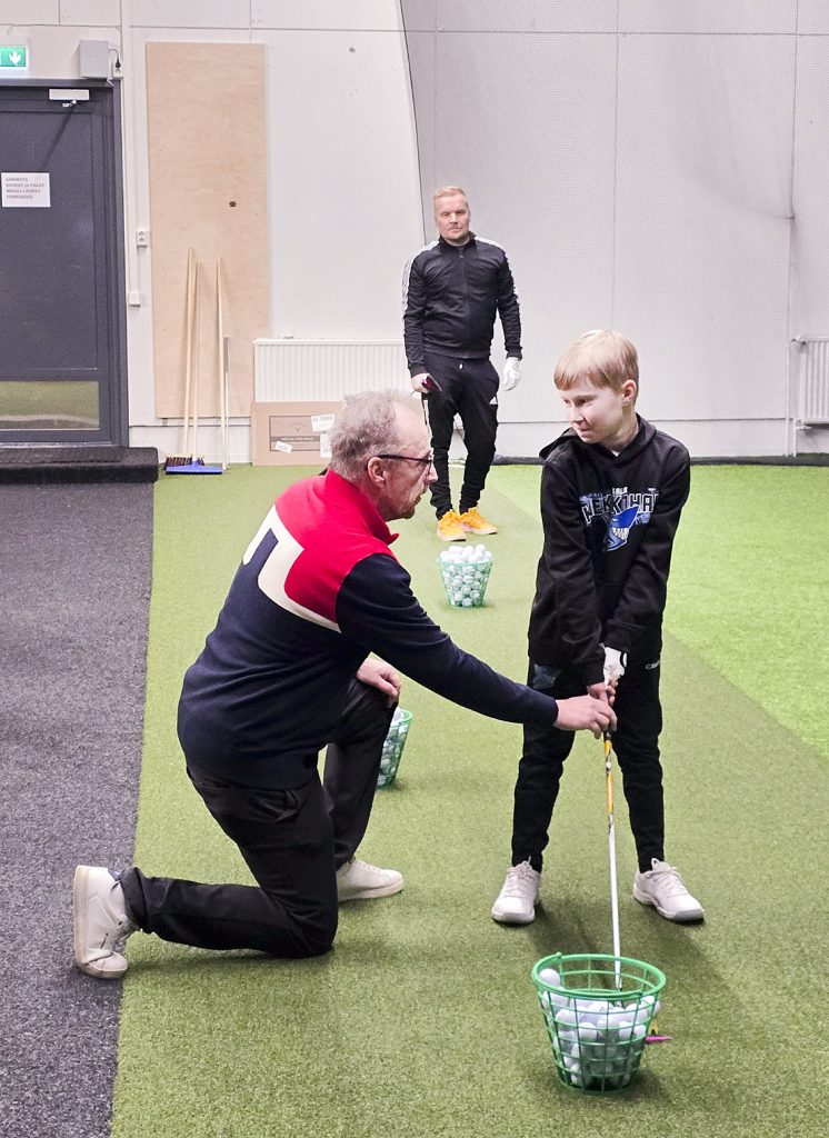 Ebi Kettunen opastaa Aaronia hyvään alkuasentoon Ollin harjoitellessa avauslyöntiä taaempana.

