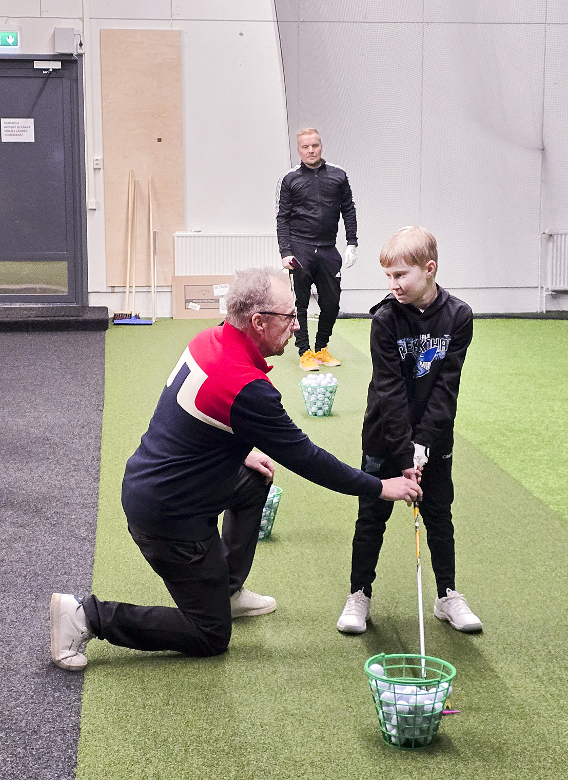 Ebi Kettunen opastaa Aaronia hyvään alkuasentoon Ollin harjoitellessa avauslyöntiä taaempana.